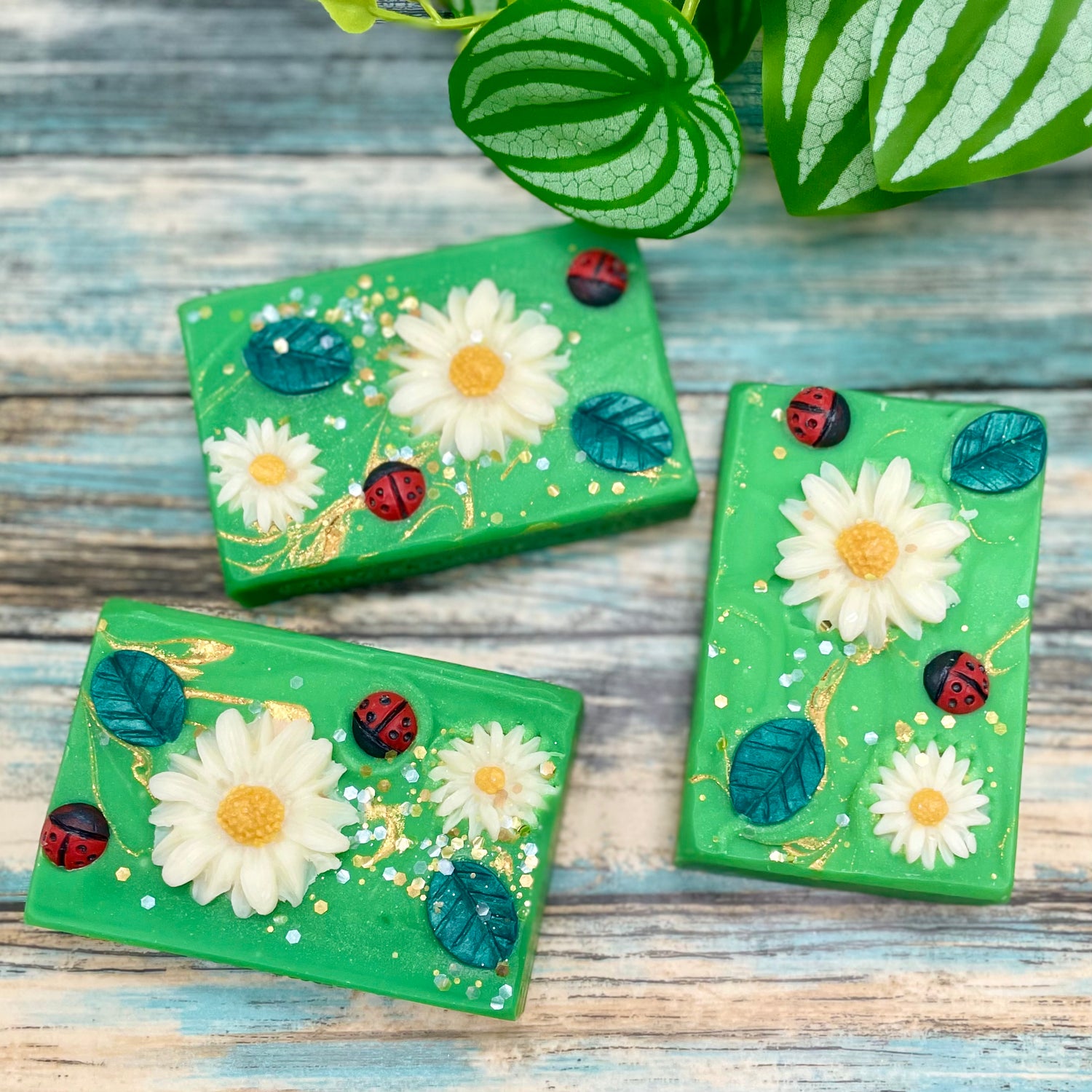 Three green decorative boxes with floral and ladybug designs on a wooden surface.