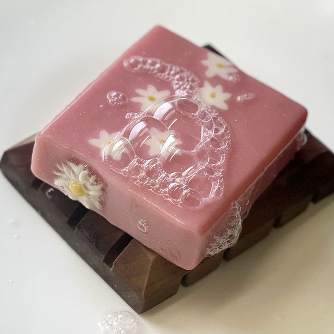 pink daisy soap with bubbles on wooden soap dish