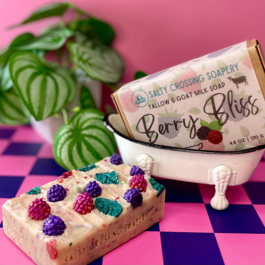 Bar of soap with berry decorations in front of a miniature bathtub and 'Salty Crossing Soapery' packaging on a checkered background.