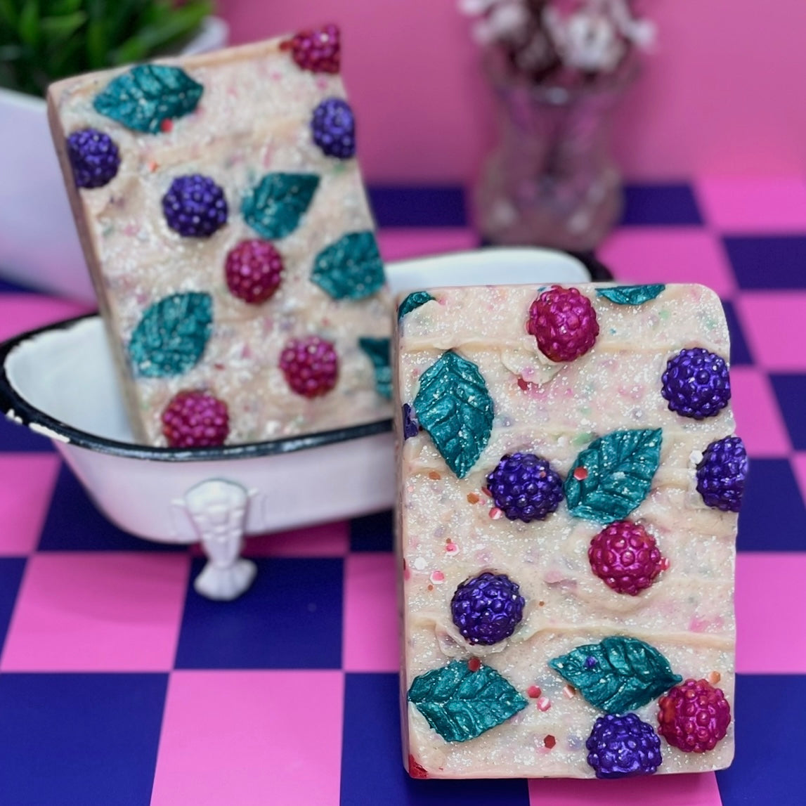 Decorative soap bars with berry and leaf patterns on a checkered pink and purple floor.