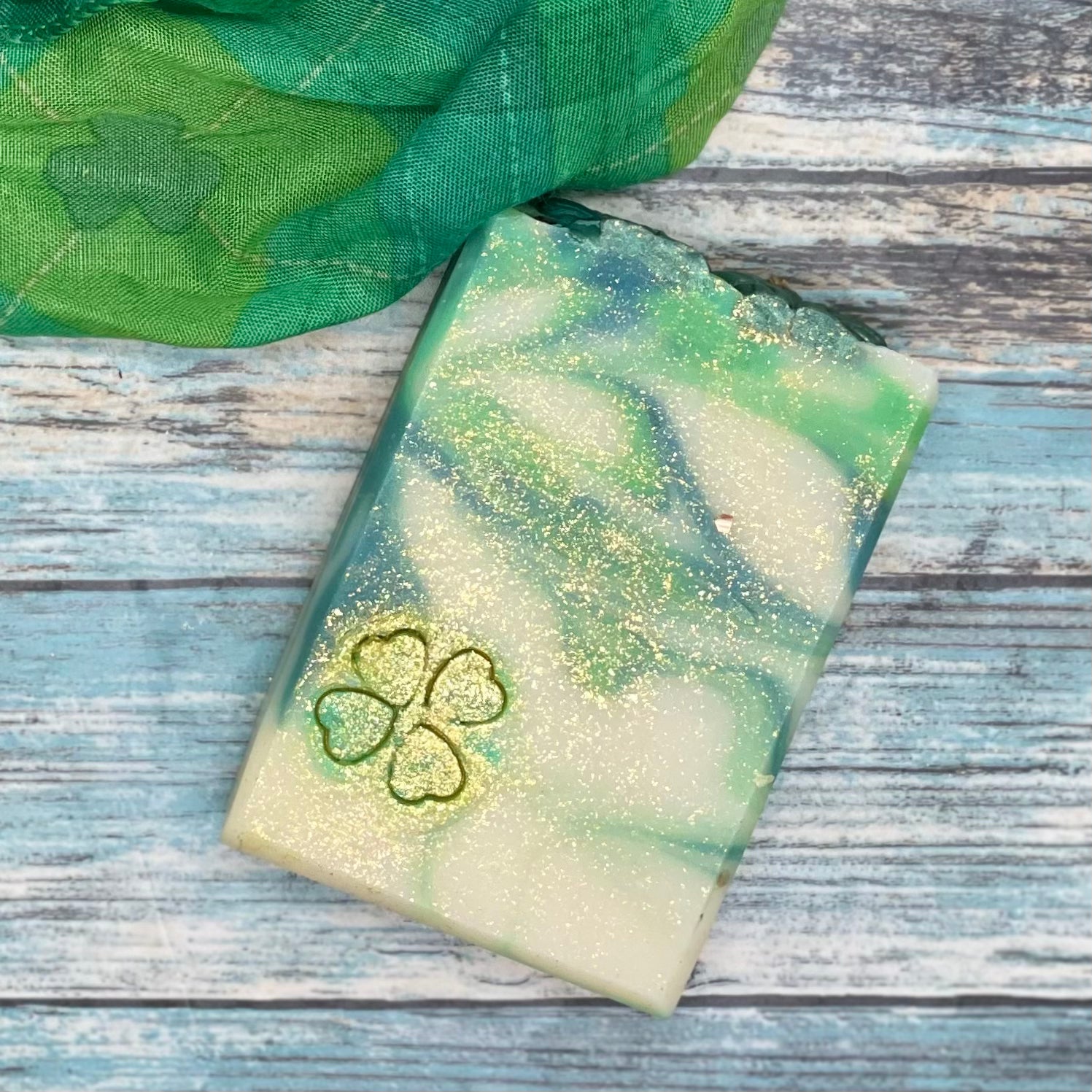 Feeling lucky handmade soap close up. Green and white swirled bar with shamrock stamp and gold dust sparkles.