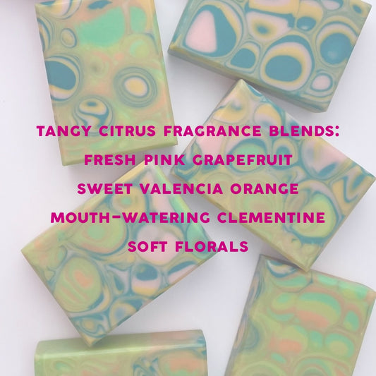 Colorful soap bars with a text overlay listing fragrance blend on a white background. Tangy Citrus Fragrance blends fresh pink grapefruit, sweet valencia orange, mouth-watering clementine, and soft florals.