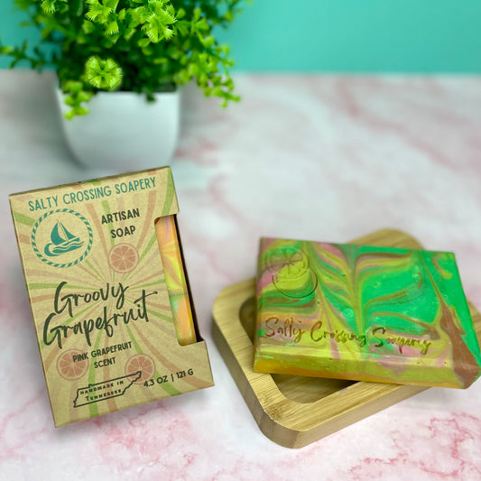 Salty Crossing Soapery artisan soap with packaging on a light surface with a plant in the background