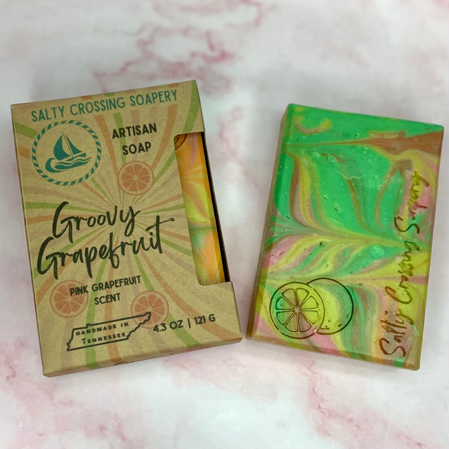 Artisan soap with marbled design and 'Salty Crossing Soapery' packaging on a pink marble background.