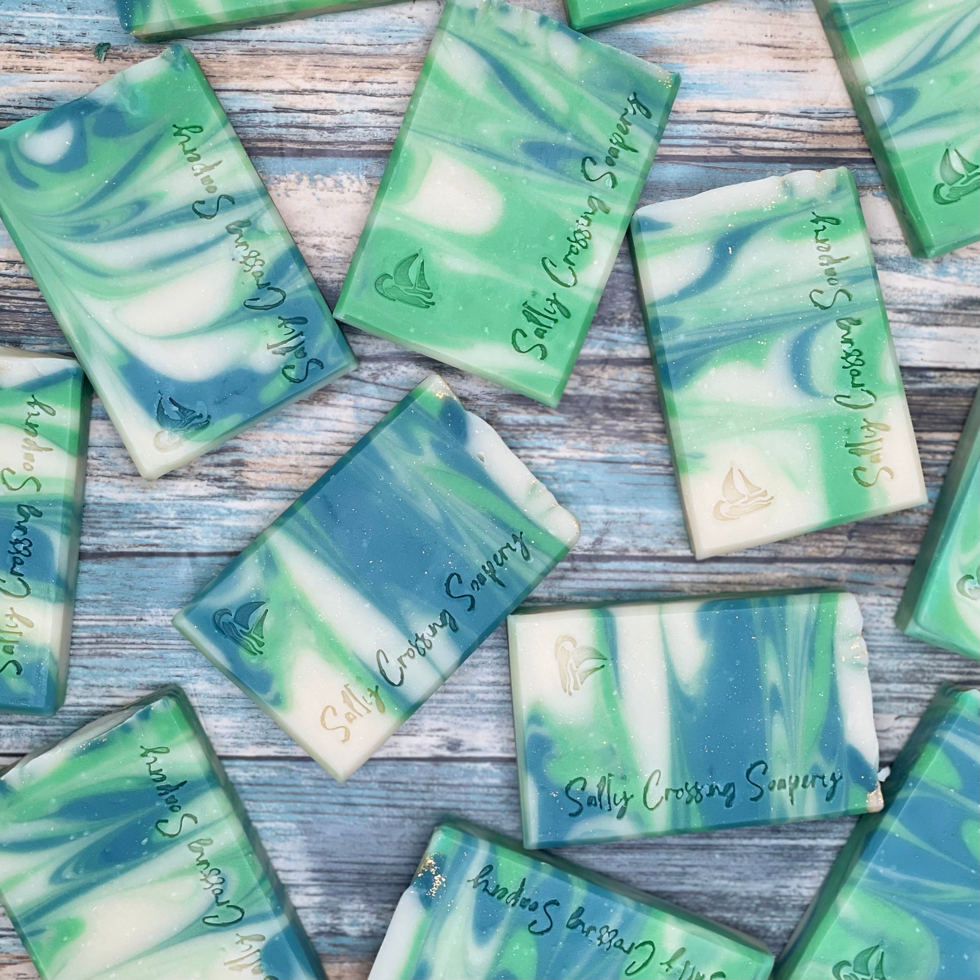 Arrangement of soap bars. Each bar is swirled with three colors-deep green, bright green, and white-and stamped with a small sailboat graphic and salty crossing Soapery text