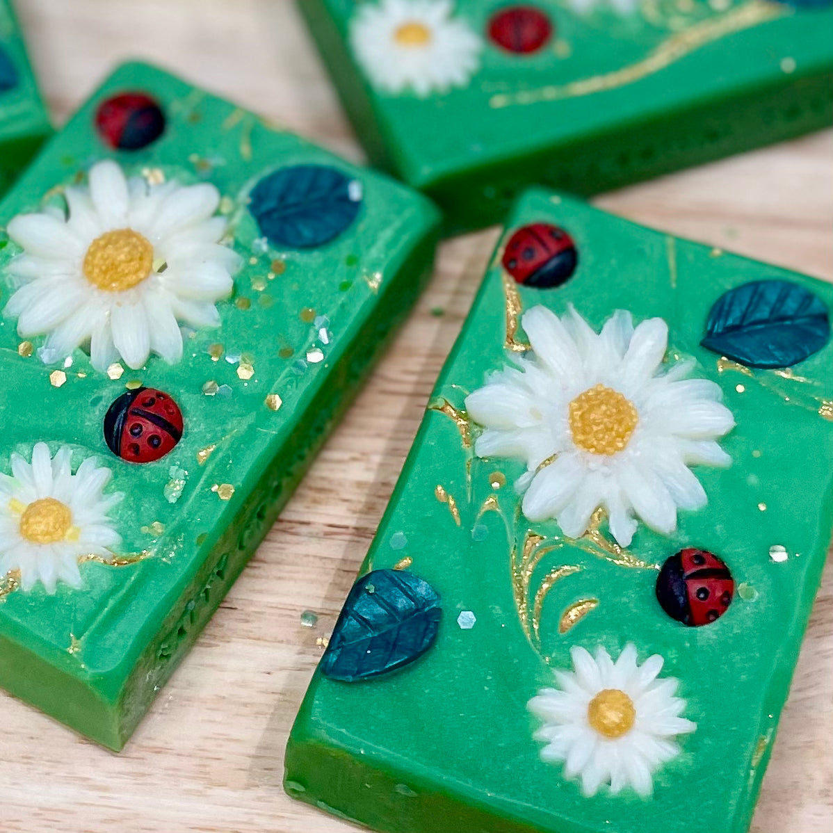 Green soap bars with floral and ladybug designs on a wooden surface