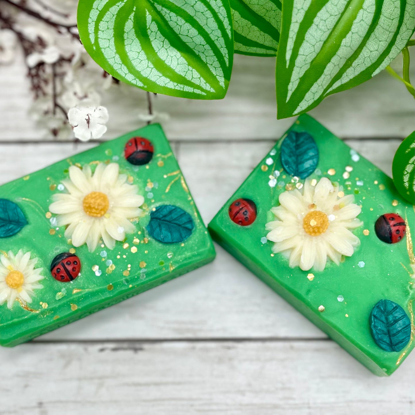 Two green soap bars with floral and ladybug designs on a wooden surface.