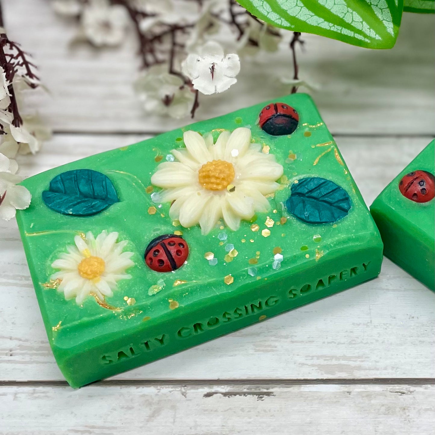 Green soap bar with floral and ladybug decorations on a wooden surface.