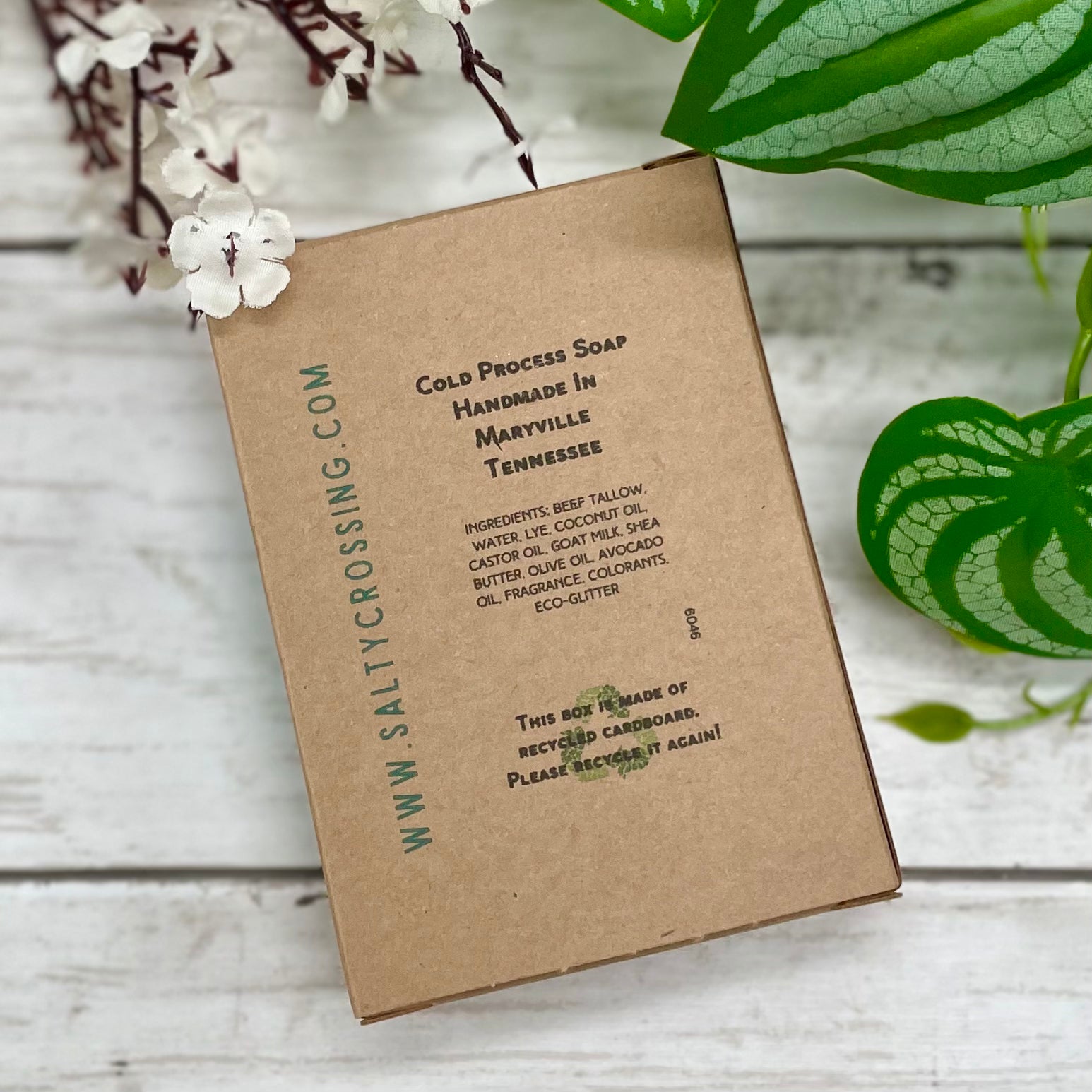 Kraft paper soap packaging with text on a wooden surface with plants.