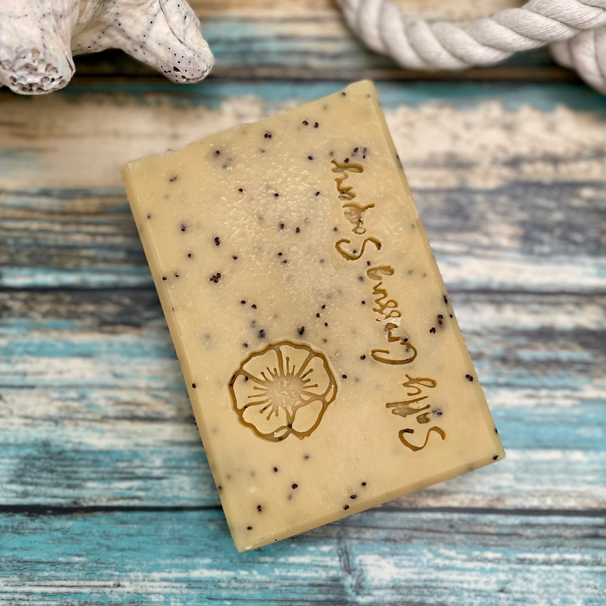 Bar of soap with specks on a wooden surface, featuring a brand logo.