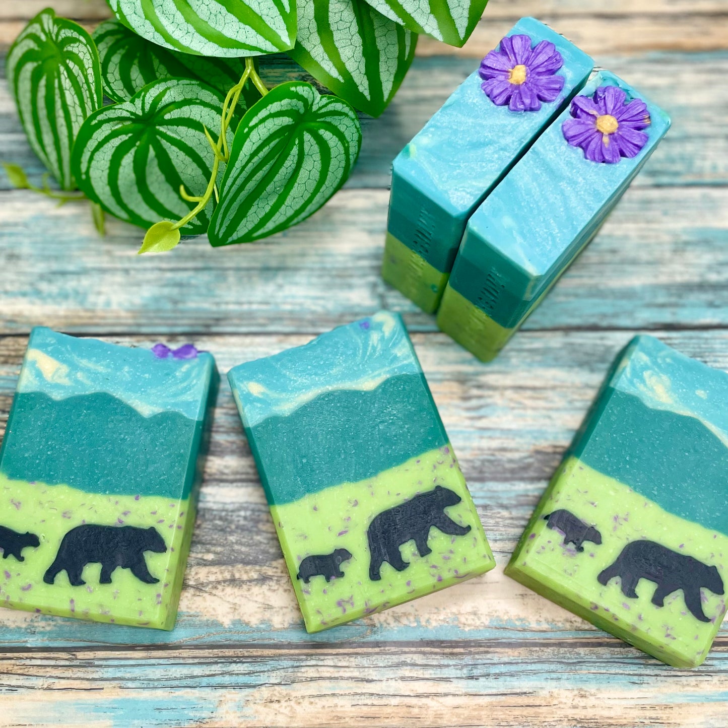 Four soap bars with bear designs on a wooden surface with green leaves in the background