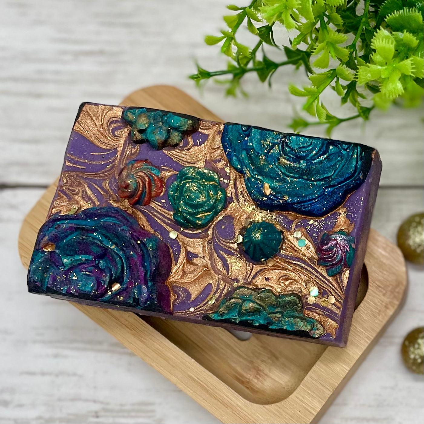 Decorative soap bar with artistic design on a wooden stand, green plant in the background