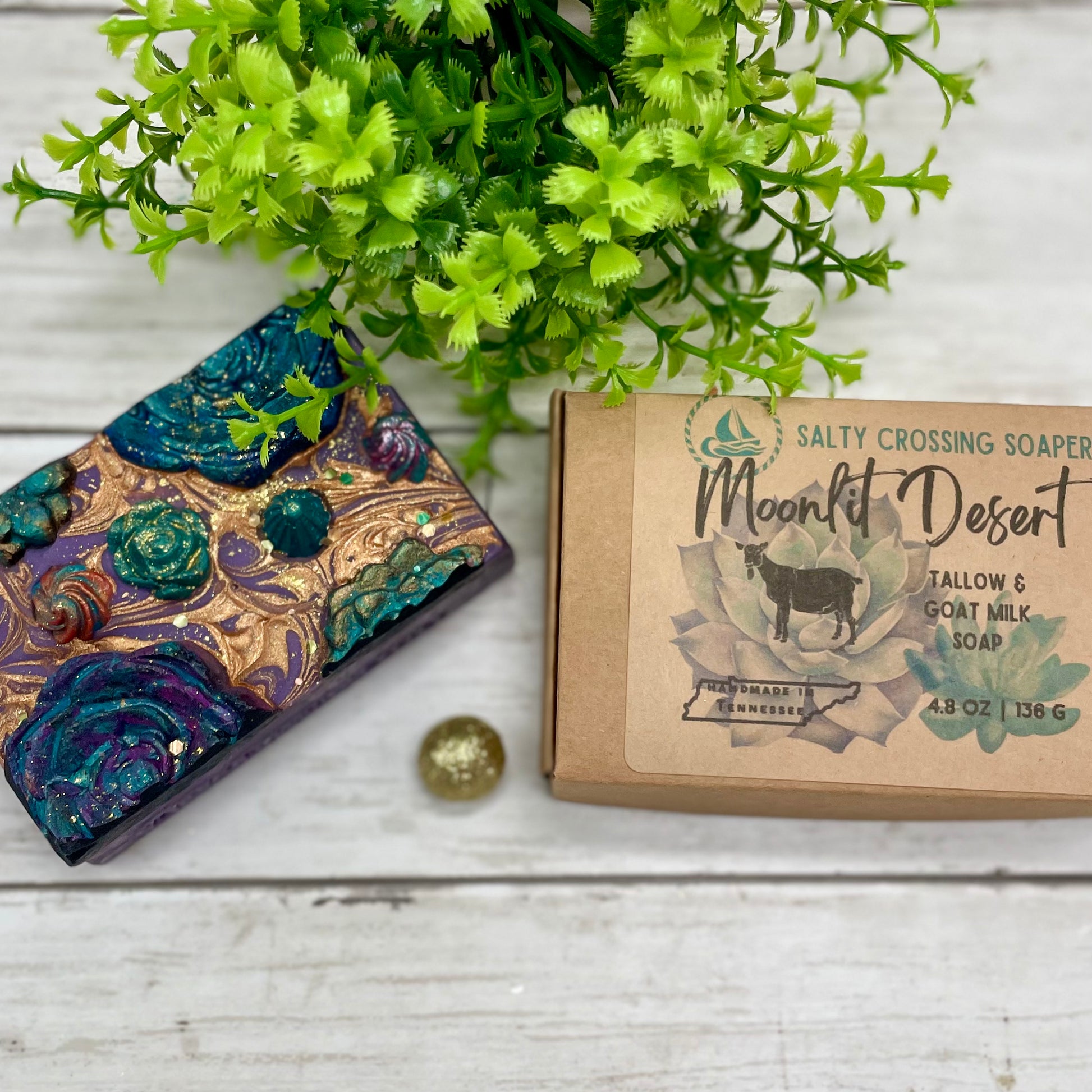 Decorative soap with a decorative box labeled 'Moonlit Desert' on a wooden surface with greenery.