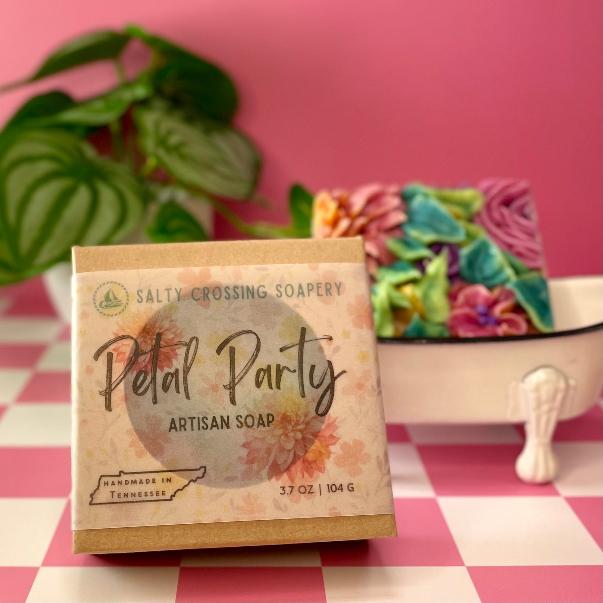 Artisan soap bar with 'Petal Party' packaging on a checkered tablecloth with a pink background.