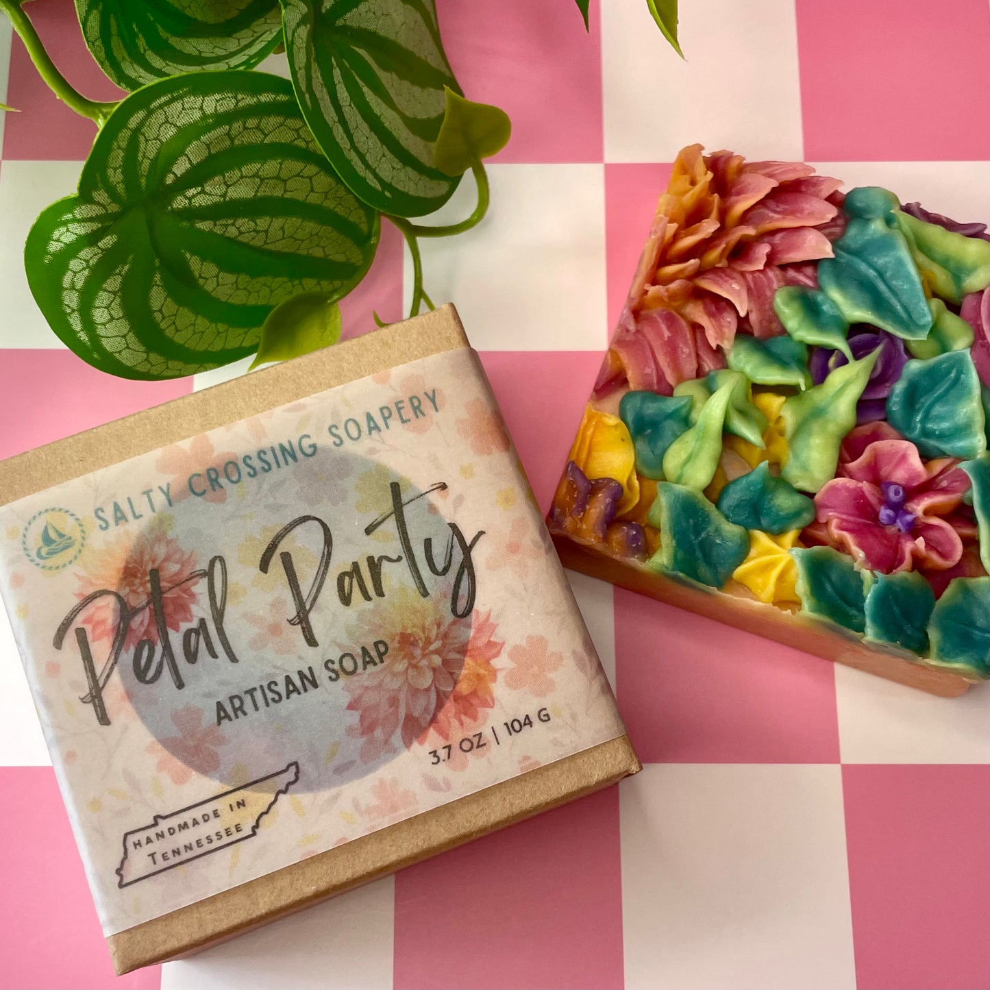 Artisan soap with colorful floral design next to its packaging on a checkered background