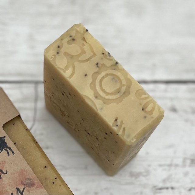 close up of soap bar showing flower texture imprint on the top. Light yellow bar with poppy seeds throughout.