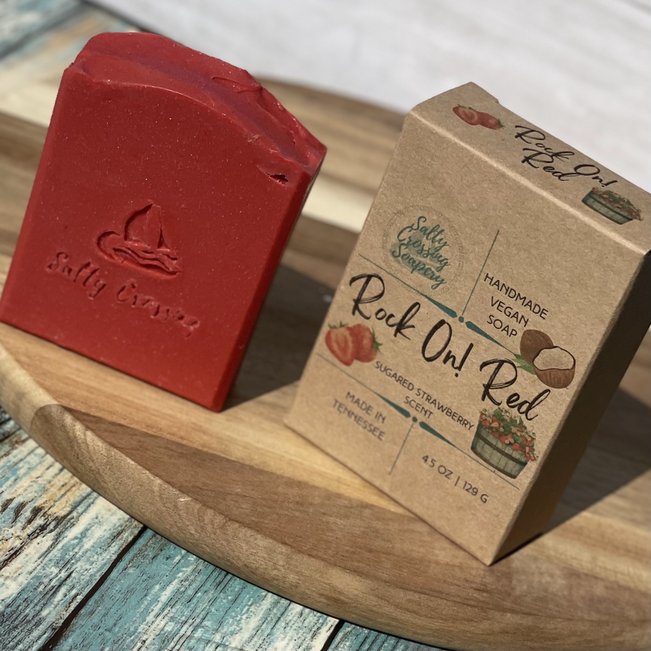 rock on! red coconut milk soap with box. red soap with sailboat and Salty Crossing stamped on front. pink sparkles throughout the bar. kraft colored box printed with strawberries and handmade in tennessee.