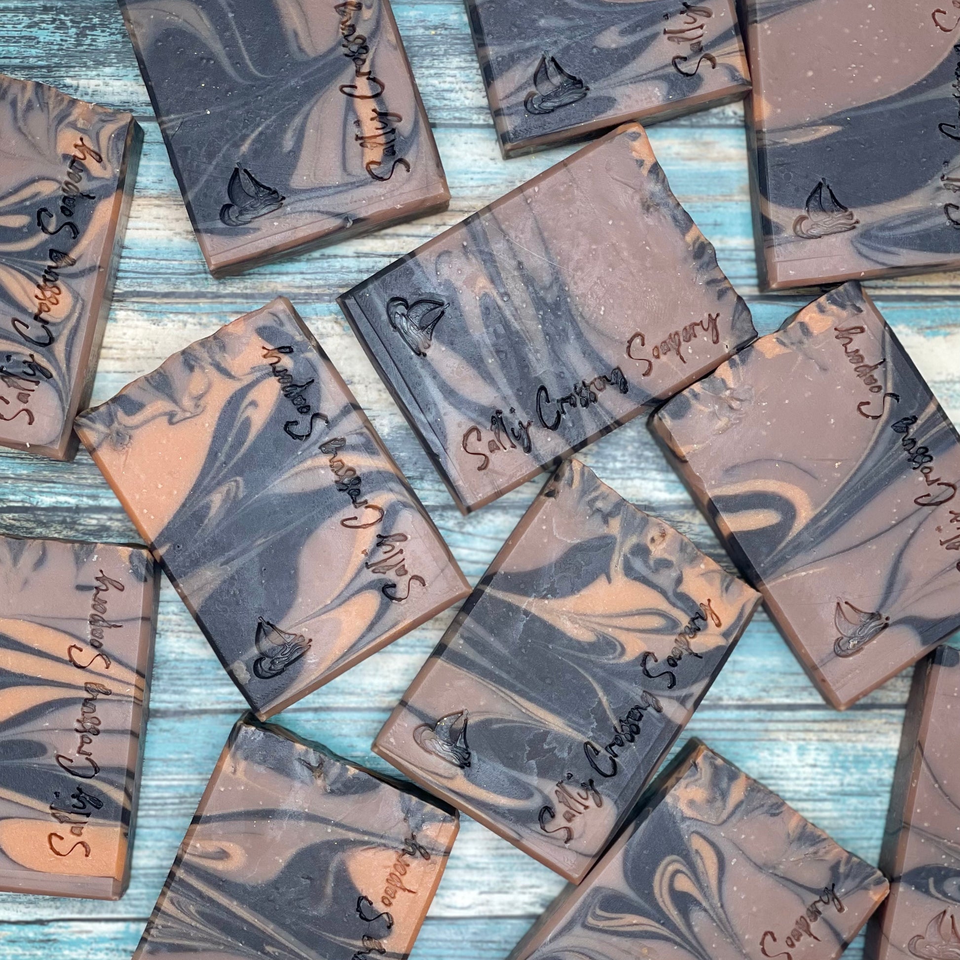 Arrangement of soap bars. Each bar is swirled with the colors-deepest brown, medium brown, and caramel- and hand stamped with a small sailboat graphic and salty crossing Soapery text