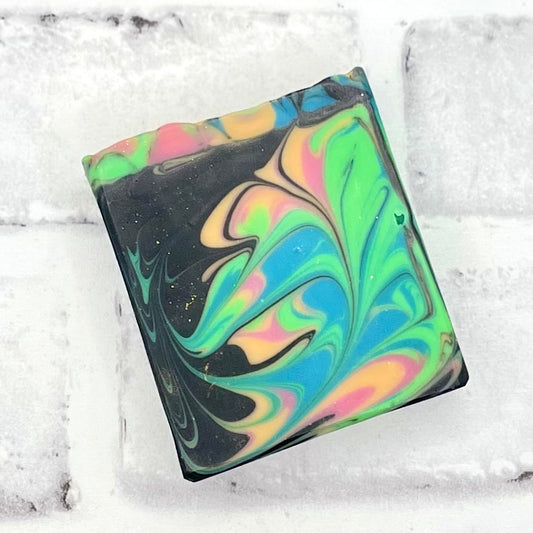 Black soap with colorful feather like swirl in green blue gold and pink. 